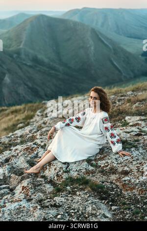 Frau in traditioneller Kleidung sitzt barfuß auf einem Berggipfel. Stockfoto