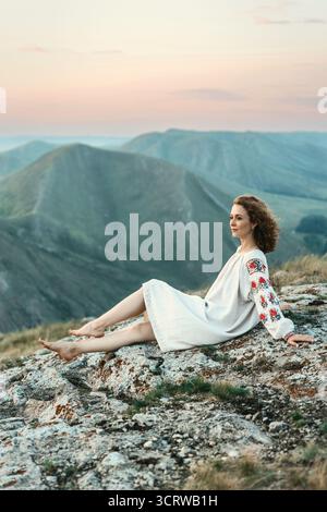 Frau in traditioneller Kleidung sitzt barfuß auf einem Berggipfel. Stockfoto