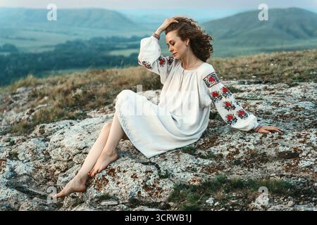 Frau in traditioneller Kleidung sitzt barfuß auf einem Berggipfel. Stockfoto