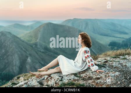 Frau in traditioneller Kleidung sitzt barfuß auf einem Berggipfel. Stockfoto