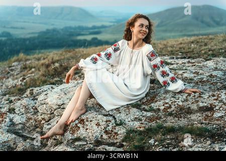 Frau in traditioneller Kleidung sitzt barfuß auf einem Berggipfel. Stockfoto