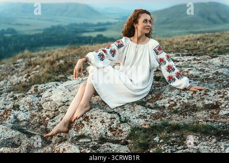 Frau in traditioneller Kleidung sitzt barfuß auf einem Berggipfel. Stockfoto