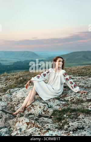 Frau in traditioneller Kleidung sitzt barfuß auf einem Berggipfel. Stockfoto