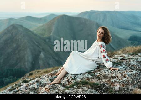 Frau in traditioneller Kleidung sitzt barfuß auf einem Berggipfel. Stockfoto