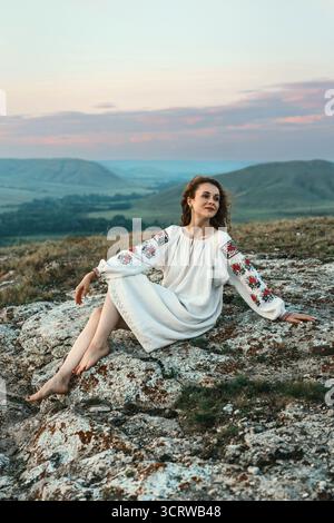 Frau in traditioneller Kleidung sitzt barfuß auf einem Berggipfel. Stockfoto
