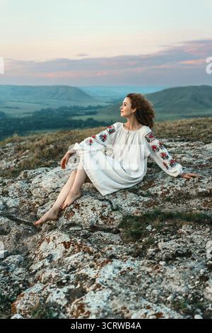 Frau in traditioneller Kleidung sitzt barfuß auf einem Berggipfel. Stockfoto