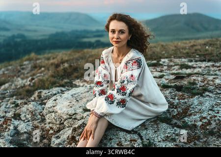 Frau in traditioneller Kleidung sitzt barfuß auf einem Berggipfel. Stockfoto