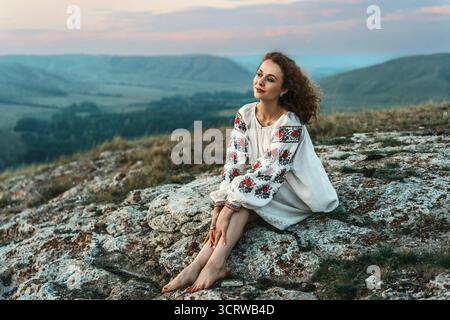 Frau in traditioneller Kleidung sitzt barfuß auf einem Berggipfel. Stockfoto