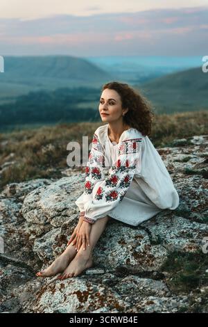 Frau in traditioneller Kleidung sitzt barfuß auf einem Berggipfel. Stockfoto