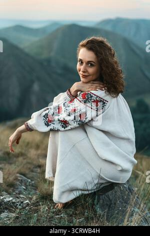 Frau in traditioneller Kleidung sitzt barfuß auf einem Berggipfel. Stockfoto