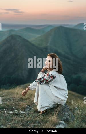 Frau in traditioneller Kleidung sitzt barfuß auf einem Berggipfel. Stockfoto