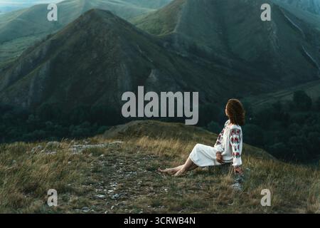 Frau in traditioneller Kleidung sitzt barfuß auf einem Berggipfel. Stockfoto