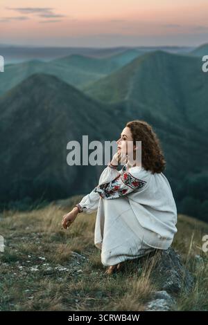 Frau in traditioneller Kleidung sitzt barfuß auf einem Berggipfel. Stockfoto
