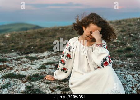 Frau in traditioneller Kleidung sitzt barfuß auf einem Berggipfel. Stockfoto