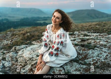 Frau in traditioneller Kleidung sitzt barfuß auf einem Berggipfel. Stockfoto