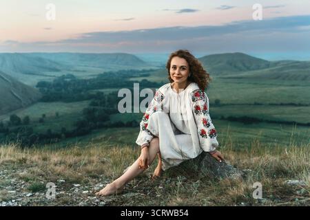 Frau in traditioneller Kleidung sitzt barfuß auf einem Berggipfel. Stockfoto