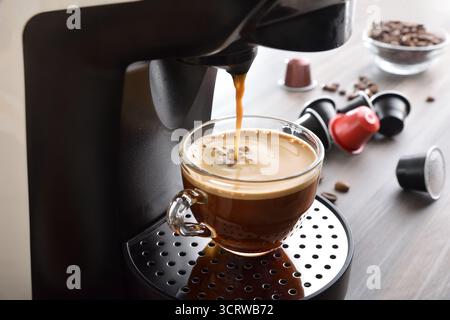 Kaffeemaschine für die Zubereitung von Espresso in einer Glasschale auf einer hölzernen Küchenbank mit Kaffeekapseln und. Erhöhte Aussicht. Stockfoto