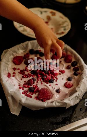 Geben Sie gefrorene Beeren von Hand auf cremiges Joghurt-Dessert Stockfoto