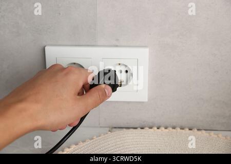 Mann, der drinnen den Stecker in die Steckdose steckt, Nahaufnahme Stockfoto