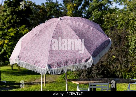 Ein stilvoller Dachschirm mit hübschem Blumendesign und dekorativem Fransen steht hoch in einem lebendigen Garten. Es bietet Schatten und Charme für jeden Outd Stockfoto