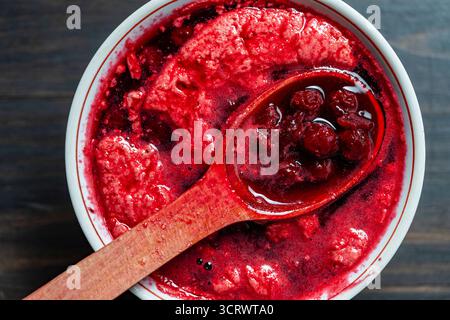 Zubereitung frisch gepflückter roter Kirschen mit Zucker, um Kirschmarmelade in einer weißen Schüssel mit einem Holzlöffel zu machen. Kochen Beeren-Marmelade, Hauskeks Stockfoto