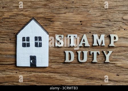 Inschrift Stempelgebühr aus Holzbriefen neben Holzhaus, Draufsicht, Nahaufnahme. Stempelsteuer ist eine Steuer, die auf den Kauf von Immobilien oder Grundstücken erhoben wird Stockfoto