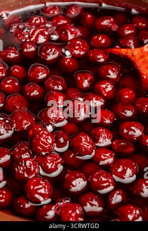 Zubereitung frisch gepflückter roter Kirschen mit Zucker zu Kirschmarmelade in einem Topf mit einem Holzlöffel, Nahaufnahme. Kochen Beeren Marmelade, hausgemachte Kekse Stockfoto