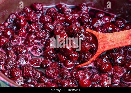 Zubereitung frisch gepflückter roter Kirschen mit Zucker zu Kirschmarmelade in einem Topf mit einem Holzlöffel, Nahaufnahme. Kochen Beeren Marmelade, hausgemachte Kekse Stockfoto