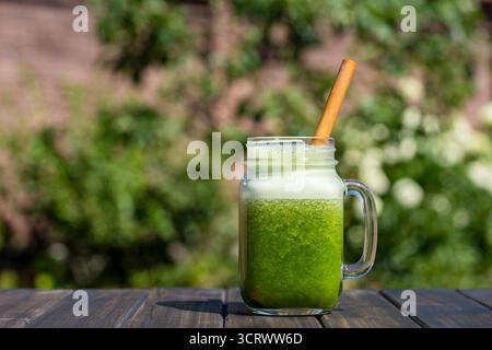 Frischer grüner Smoothie in einem Glasbecher mit Bambusstroh vor Sommergartenhintergrund auf Holztisch, Nahaufnahme. Konzept der gesunden Ernährung. Detox dri Stockfoto
