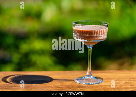 Köstlicher Schokoladencocktail serviert in einem eleganten Kristallglas mit grünem Sommergarten Hintergrund, Nahaufnahme, Kopierraum. Perfekt für Partys im Freien Stockfoto