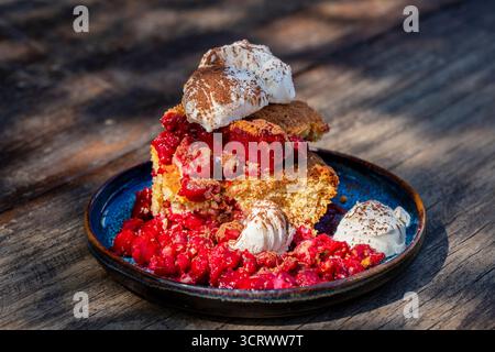Weißer Teller mit frisch gebackenem Kirschschuster und Vanilleeis auf einem Holztisch in einem Straßencafé an einem sonnigen Sommertag im Freien, in der Nähe von Stockfoto