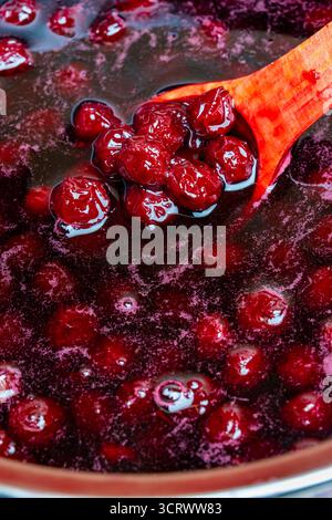 Zubereitung frisch gepflückter roter Kirschen mit Zucker zu Kirschmarmelade in einem Topf mit einem Holzlöffel, Nahaufnahme. Kochen Beeren Marmelade, hausgemachte Kekse Stockfoto