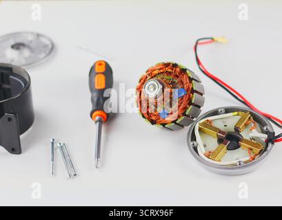 Diese Abbildung zeigt zerlegte Teile des Elektromotors, einschließlich des Stators mit Kupferspulen und des Rotors, die mit einem Schraubendreher und auf einer weißen Oberfläche platziert werden Stockfoto