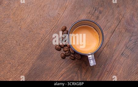 Verstreute Kaffeebohnen mit Espresso, serviert in einem Glasbecher. Die cremige Crema auf dem Espresso verleiht dem Espresso einen optischen Reiz. Stockfoto