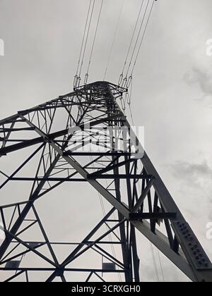 Stahlkraftübertragungsturm gegen bewölkten Himmel. Eine Ansicht der geometrischen Struktur der Metallträger aus einem niedrigen Winkel erzeugt ein Gefühl der Industrie. Stockfoto