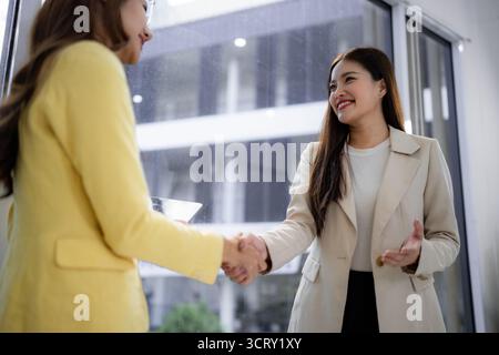 Zwei erwachsene asiatische Geschäftsfrauen schließen durch Handschlag in einer modernen Büroumgebung ein gegenseitiges Vertrauensabkommen Stockfoto