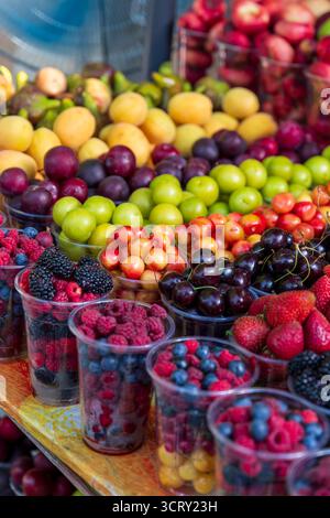 A vibrant assortment of fresh berries, plums, cherries, and apricots, beautifully displayed in cups at a bustling market stall Stockfoto