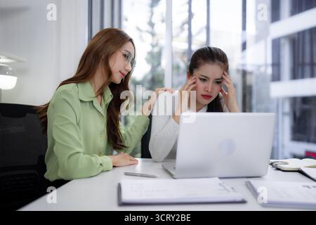 Zwei Erwachsene asiatische Frauen unterstützen einen gestressten Kollegen, der sich mit einem schwierigen Geschäftsproblem am Arbeitsplatz konfrontiert sieht, einfühlsam Stockfoto