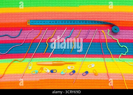 Alles für Handstricke. Gestrickter mehrfarbiger handgefertigter Stoff mit Kugeln aus mehrfarbigen Garnen, Stoffmessgerät, Nadeln und diversen Stricknetzen Stockfoto