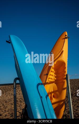 Farbenfrohe Kajaks an einem Kieselstrand unter klarem blauen Himmel in West Bay, Dorset, England. Stockfoto