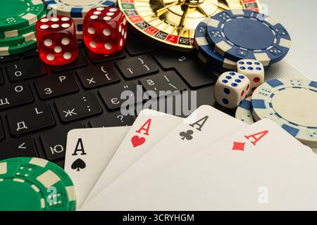 Ein lebhaftes Bild, das Online-Spiele zeigt, mit einem Laptop-Bildschirm, auf dem Poker-Karten und traditionelle Casino-Gegenstände wie Chips, Würfel und Karten Sy angezeigt werden Stockfoto