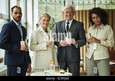 Gruppe von verschiedenen Geschäftsleuten, einschließlich Kaukasierin mittleren Alters, älterer Kaukasier, junger Erwachsener Schwarzer Frau, junger Erwachsener Mann, der zusammen mit Champagner steht Stockfoto