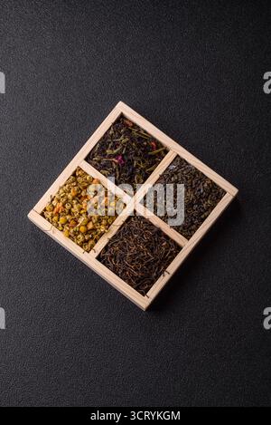 Eine Holzkiste mit verschiedenen Arten von getrocknetem Tee, grünem, schwarzem, Obst und Kamille. Trockener Tee in der Box als Hintergrund für Ihr Design. Stockfoto