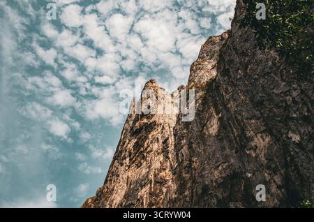 Hoch aufragende Felswände vor einem bewölkten blauen Himmel - dramatische Aussicht aus dem niedrigen Winkel Stockfoto