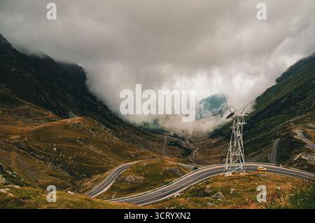 In großer Höhe kurvige Bergstraße und Seilbahnturm, umgeben von dramatischem Nebel Stockfoto