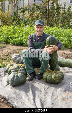 Der Mensch ist glücklich mit seiner Kürbisernte, sitzt im Garten und lächelt Stockfoto