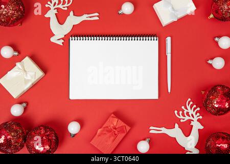 Weihnachtskomposition von Geschenkboxen und Spielzeug auf dem Weihnachtsbaum, mit offenem leerem Notizbuch und Stift auf rotem Hintergrund zum Schreiben von Zielen und Plänen für das neue Jahr. Flache Ladefläche, Kopierraum Stockfoto
