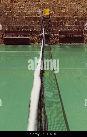 Tennisplatz in Heraklion, Griechenland, mit einem zentrierten Netz, einem gelben Schiedsrichter-Stuhl und einer Steinmauer im Hintergrund – eine ruhige Mischung aus Sport und altem Archite Stockfoto