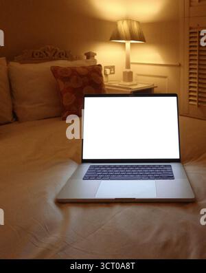 Laptop mit leerem weißen Bildschirm, der auf einem Bett in gemütlicher Schlafzimmeratmosphäre steht und als Symbol für Arbeit oder Entspannung außerhalb der Ferne dient. Modellkopierraum Stockfoto