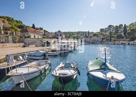 Eine ruhige Hafenszene mit vertäuten Booten, klarem blauem Wasser und sonnendurchfluteten Steinhäusern an einem mediterranen Dorfufer. Ideal für Reisen, Freizeit und Stockfoto